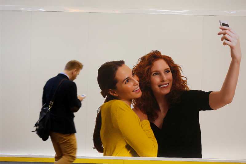 Two women taking a selfie with a man walking past in background